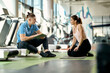 Happy athletic woman talking to her personal trainer during break in a gym.