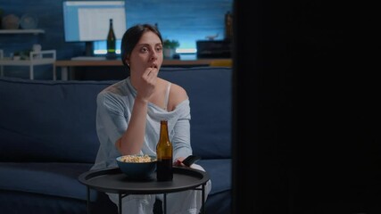 Wall Mural - Emotional young woman eating popcorn while watching disgusting tv program movie alone in living room, feeling confused shocked about horror film, violence in social media, awful news or morbid shows.