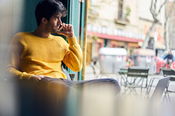 Wall Mural - Thoughtful young man sitting in cafe and talking on smartphone