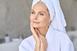 © insta_photos - Happy beautiful middle aged woman wearing bathrobe and white towel with perfect complexion touching face looking away in bathroom. Advertising of skin care spa wellness concept. Closeup portrait.