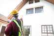 © SUPERMAO - A male engineer inspects the house to deliver it to the customer. Standing in front of the house, pointing to the front. concept of house construction residential building