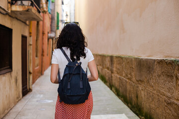 Wall Mural - Rear view of a young woman with a backpack walking down a lonely city alley