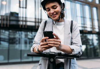 Wall Mural - Close up of businesswoman hands holding smartphone while standing on electric scooter