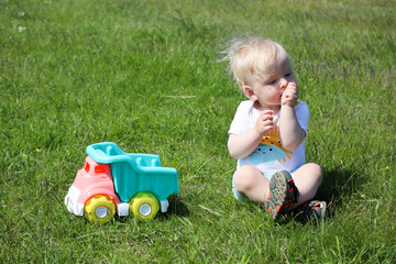 cute adorable little child playing with toy car lorry on the green grass in the park