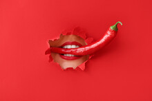 Beautiful Young Woman With Chili Pepper In Mouth Visible Through Hole In Color Paper