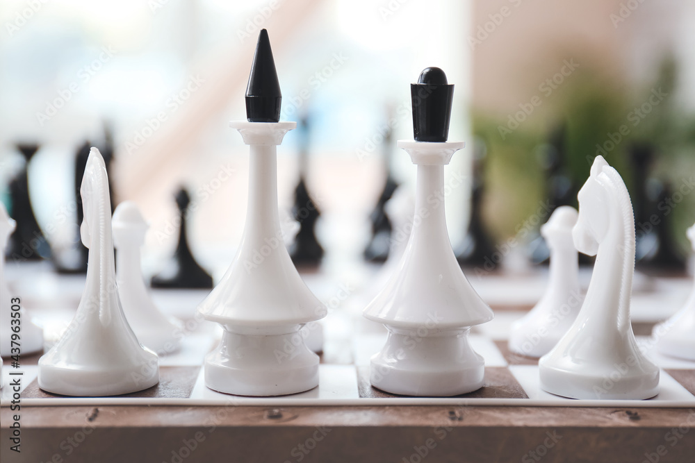 Board with chess pieces on blurred background, closeup