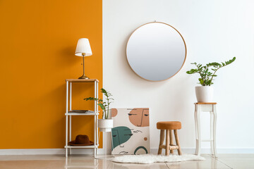 Modern lamp on table and mirror hanging on color wall in room