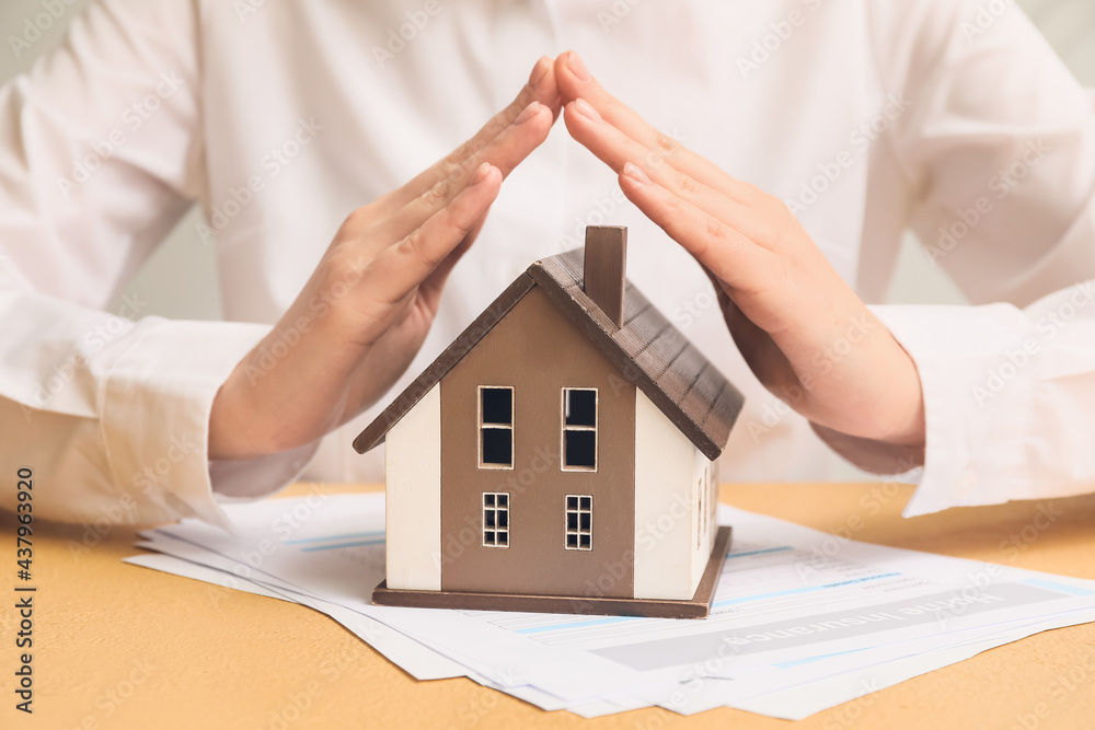 Woman with house model on color table, closeup. Property insurance concept