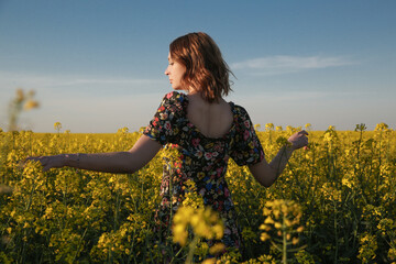 Beautiful woman in floral dress standing in field of canola