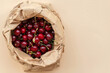 Ripe red cherries in an eco-friendly paper bag on a beige background.
