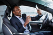 © sofiko14 - Positive male entrepreneur in business suit having mobile conversation while sitting in car with cup of coffee. African businessman solring working issues on distance.