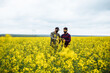 © Konstantin Zibert - Blooming rapeseed field. Two farmers in masks in the middle of the field stand with a tablet. The agronomist points to the tablet. Checking rapeseed.