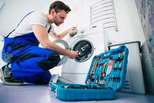 The Young Handsome Repairman In Worker Suit With The Professional Tools Box Is Fixing The Washing Machine In The Bathroom