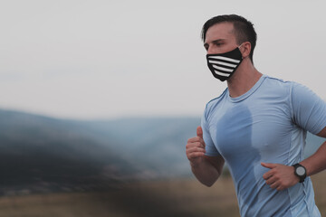 Fitness man in wet sporty clothes wearing black protective face mask running outdoors in the city during coronavirus outbreak. Covid 19 and physical jogging activity sport and fitness. New normal