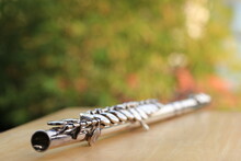 Flute, Woodwind Brass Instrument In Classical Orchestra. Silver Modern Flute On White Sheet Music Note For Education And Performance. Song Composer On Score Sheet With Green Bokeh Nature.