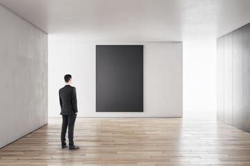 Poster - Businessman in modern concrete interior with empty poster looking at mockup place for your advertisement.