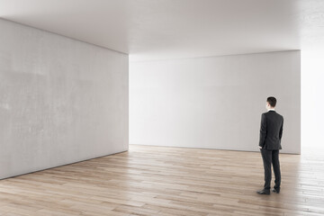 Aufkleber - Businessman in white concrete interior with empty wall looking at mockup place for your advertisement.