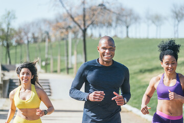 Wall Mural - Two women and a man with a mask running in a park.