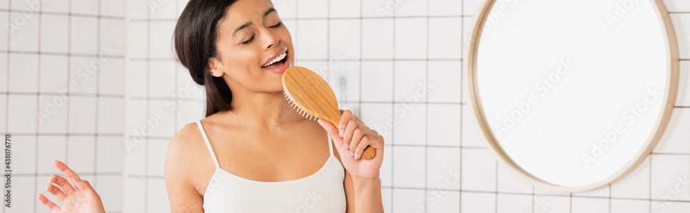 young african american woman with closed eyes singing with hair brush in bathroom, banner - obrazy, fototapety, plakaty 