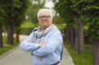 © Studio Romantic - Portrait of confident senior citizen. Elderly man in glasses and shirt standing on park pathway and looking at camera. White-haired old grandfather spending time in green park in spring or summer