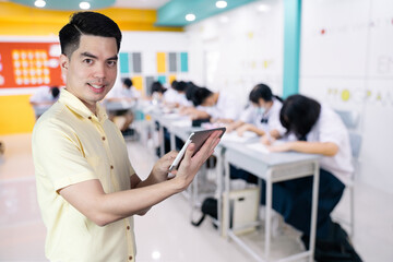 Wall Mural - Portrait handsome young asian man wearing holding smart phone or tablet feeling smile and happy isolated on background blurred student study in class at school. Education concept.