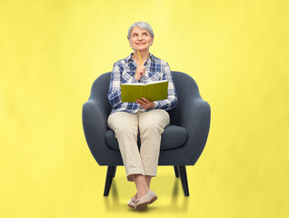 Wall Mural - inspiration, planning and old people concept - smiling senior woman sitting in modern armchair and writing to diary over illuminating yellow background