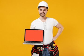 Young employee handyman man in protective helmet hardhat use laptop pc computer blank screen workspace area isolated on yellow background. Instruments renovation apartment room. Repair home concept.