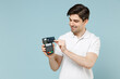 Young smiling happy man wearing white casual basic t-shirt holding wireless modern bank payment terminal to process and acquire credit card payments isolated on pastel blue background studio portrait.