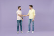 © ViDi Studio - Full length two young smiling happy men friends together in casual t-shirt meeting together greet hold hands folded handshake gesture n isolated on purple background studio People lifestyle concept