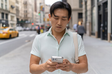 Sticker - Young Asian man in city walking using cellphone