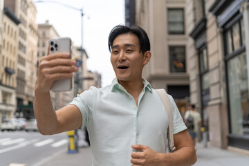 Sticker - Young Asian man in city video chat face time on cellphone walking