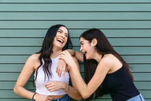 Happy Sisters Laughing Against Green Ribbed Wall