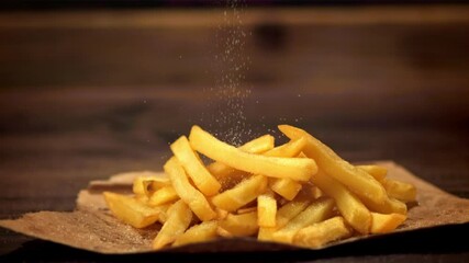 Canvas Print - Super slow motion on the French fries on paper pour salt. On a wooden background.Filmed at 1000 fps.