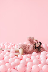 Fashion portrait of smiling pretty woman lying in many pink balloons on pink pastel background