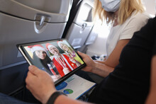 Man And Woman Celebrating Christmas With Friends In Santa Claus Hats Through Screen On Digital Tablet In Aircraft Cabin Closeup
