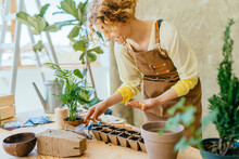 Portrait Of Happy Female Gardener Working In Home Garden Holds Seeds In The Palm And Sowing Seeds In Peat Pots In Wooden Table Indoor.