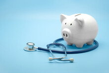 Piggy Bank With Stethoscope Isolated On Light Blue Background With Copy Space. Health Care Financial Checkup Or Saving For Medical Insurance Costs Concept.