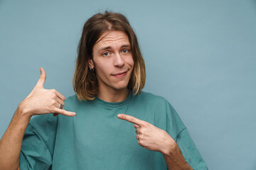 Young white man making handset gesture and pointing finger aside