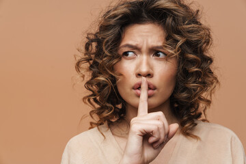 Young hispanic woman frowning while showing silence gesture at camera