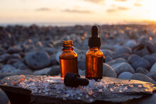 Two Bottles Of CDB Oil Standing On A Stone With Scattered Himalayan Salt Background Sunset On The Sea