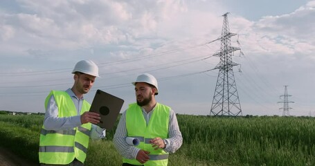 Wall Mural - two engineers look at an electronic tablet in front of a high-voltage power line, discuss transporta
