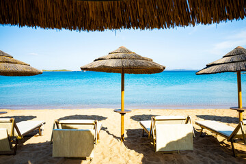 Canvas Print - (Selective focus) Stunning view of some thatch umbrellas and sun chairs on a beach bathed by a beautiful, turquoise sea. Sardinia, Italy.