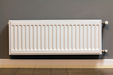 white metal heating radiator mounted on gray wall inside a room.