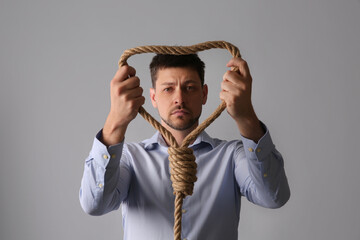 Depressed man with rope noose on light grey background