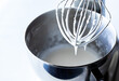 © Carey - Close up of a whisk raised out of a metal mixing bowl dripping with royal icing.
