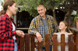 Portrait of young man, woman and little girl standing in garden near wooden fence and friendly talking