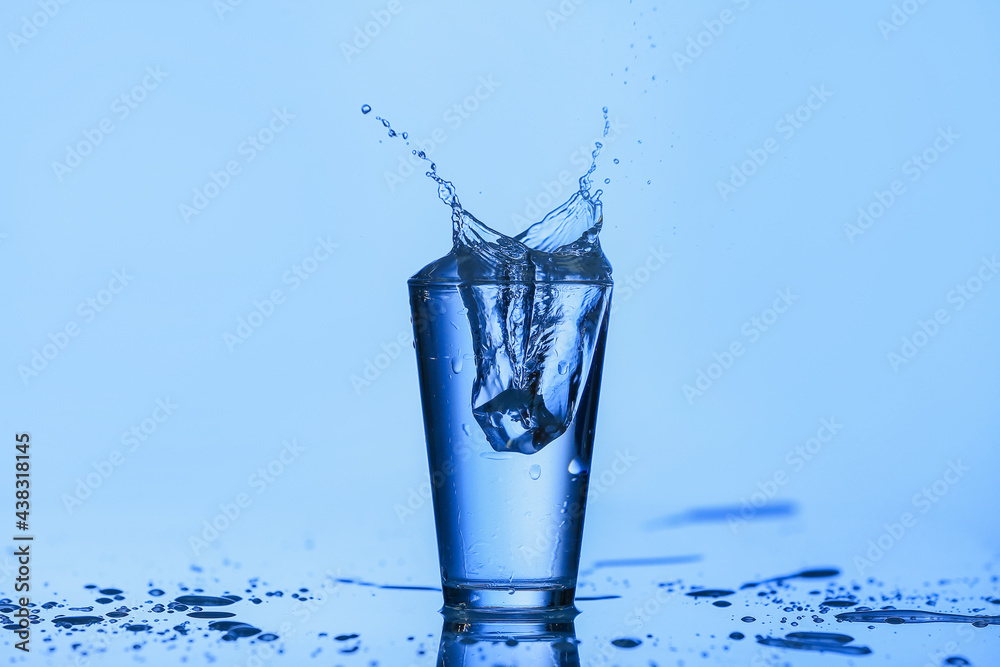 Glass of water with splash on color background