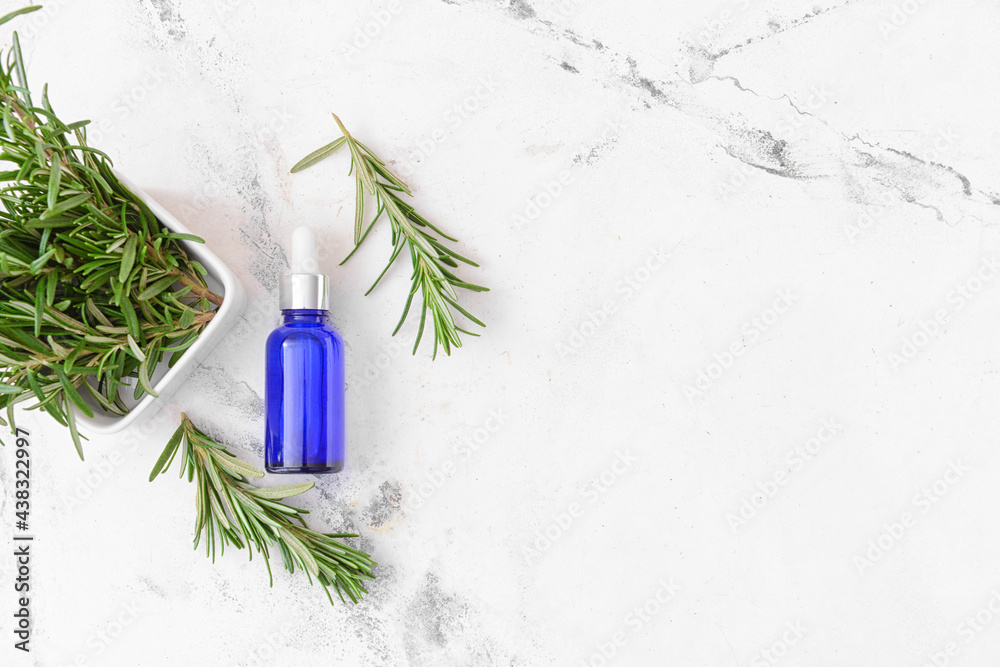 Bottle of essential oil and fresh rosemary on light background