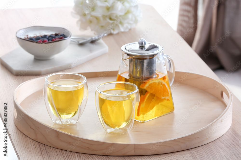 Teapot and glasses with hot beverage on tray in room