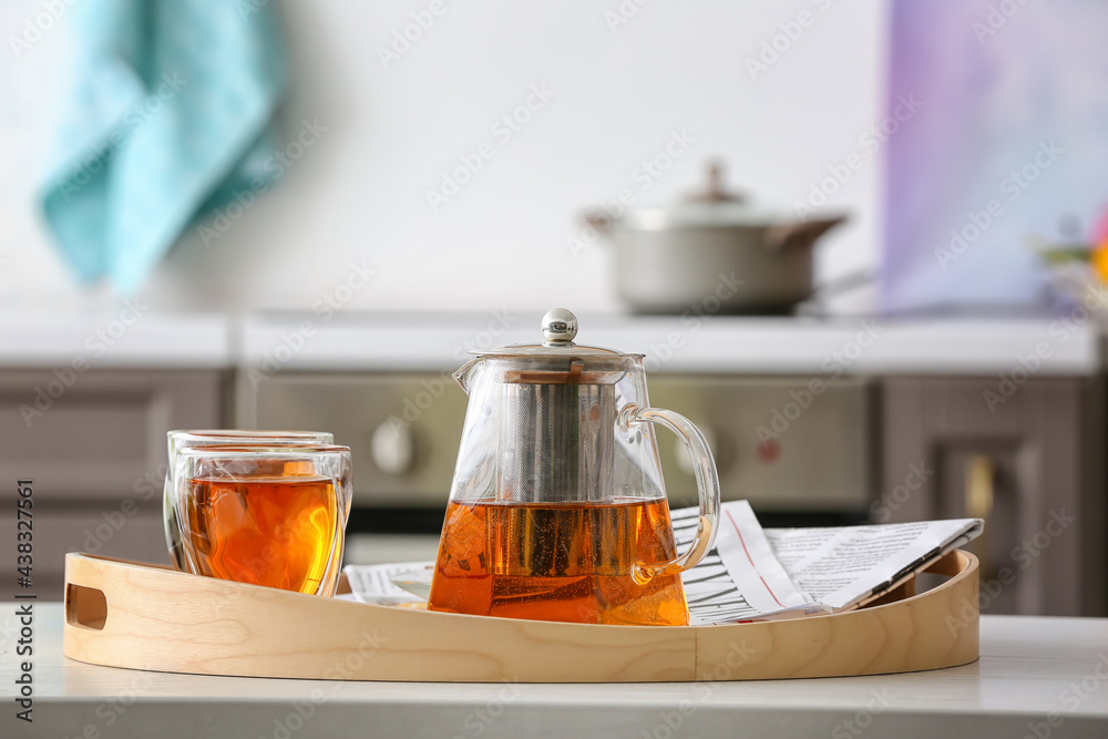 Teapot and cups of hot beverage on table in room